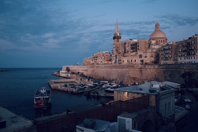 View of buildings by sea against sky in city