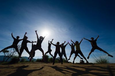 Silhouette people jumping on land against sky