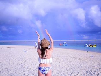 Rear view of woman gesturing while standing at beach against sky