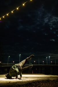 Side view of woman lying down on street against sky at night