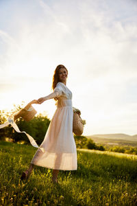 Rear view of woman standing on field against sky during sunset