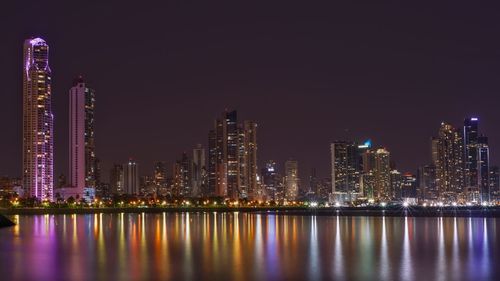 Illuminated city by buildings against sky at night