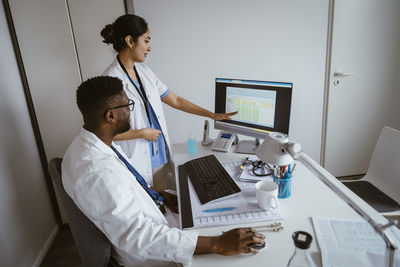 Female doctor explaining strategy to male colleague over desktop pc at healthcare center