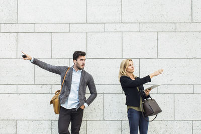 Business colleagues pointing opposite directions against wall outdoors