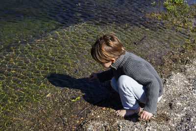 Boy crouching at lakeshore
