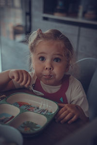 Portrait of a girl sitting on table and eats 