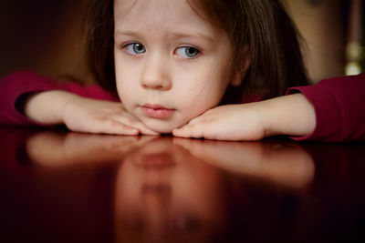Sad head of a little girl lies on the table, thinks, upset, offended, face reflection