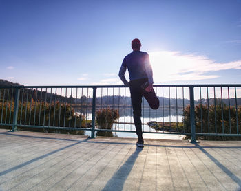 Rear view of man on footpath by railing against sky
