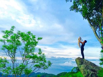 Low angle view of woman standing on tree against sky