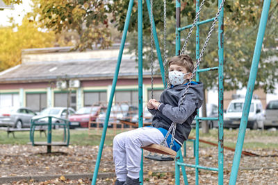 Cute kid with protective face mask swinging while spending a day at the park.