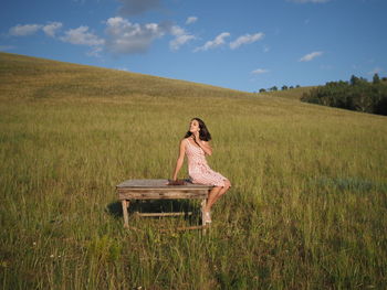 Rear view of woman sitting on field against sky