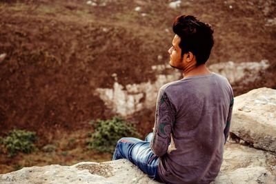 Rear view of man sitting on rock