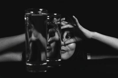 Close-up of woman gesturing over eyes seen through glasses of water 