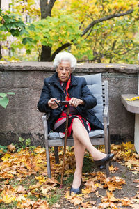 Full length of senior woman holding walking cane while sitting on chair in park
