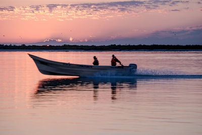 Silhouette men in boat against sky during sunset