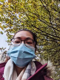 Close-up portrait of young woman wearing facemask against trees