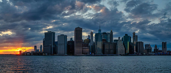 Sea by modern buildings against sky during sunset