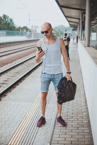 Young man in a t-shirt on the platform waiting for a train using mobile phone. man by train station 
