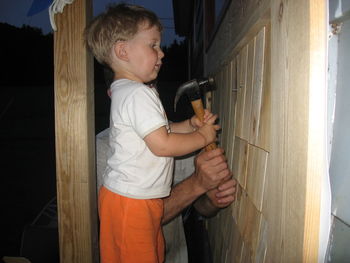 Father teaching son while hammering on wooden wall
