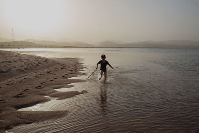 Boy walking on beach against sky