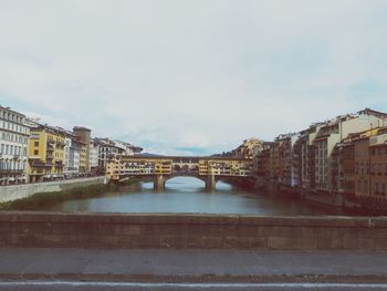 Bridge over river by buildings against sky in city