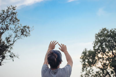 Rear view of woman with arms raised against sky