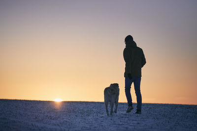 Silhouette woman standing at beach against sky during sunset