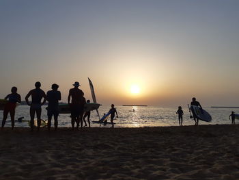 Silhouette people on beach against sky during sunset