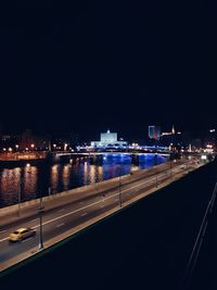 Illuminated city by river against sky at night