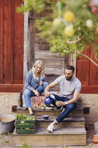 Friends talking while sitting with vegetables crate outside wooden cottage