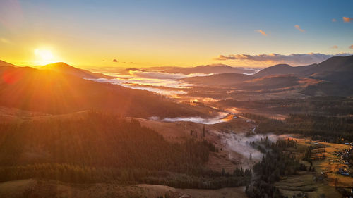 Colorful autumn sunrise foggy woodland. mountain forest cloud covered . fall rural  village  valley