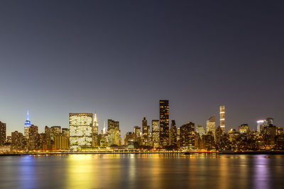 Illuminated buildings by river against sky in city at night