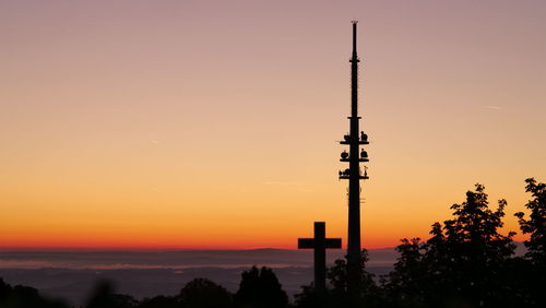 Silhouette of communications tower and cross against sky during sunrise