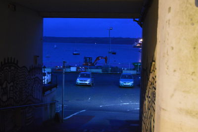 Cars on illuminated road by sea against blue sky at night