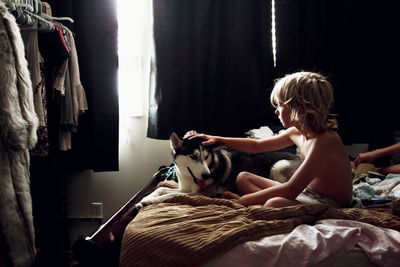 Shirtless boy touching siberian husky dog on bed