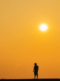Silhouette man standing on land against orange sky