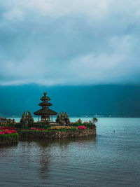 Illuminated building by sea against cloudy sky