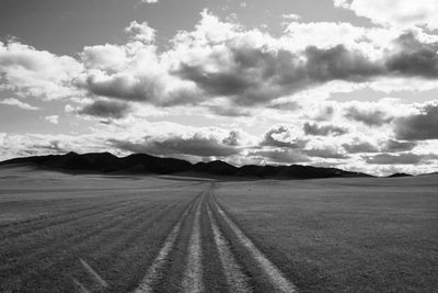 View of road passing through field against cloudy sky