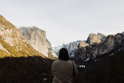 Rear view of man looking at rock formation against sky