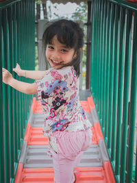 Portrait of cute smiling girl climbing on outdoor play equipment