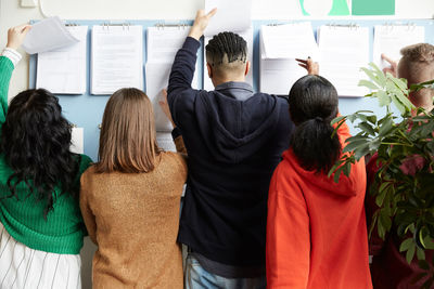 Rear view of university students checking bulletin board for test result