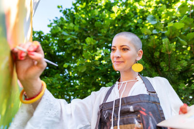 Beautiful young woman relaxing while painting an art canvas outdoors in her garden. 