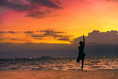 Full length of silhouette young woman practicing yoga on shore at beach during sunset