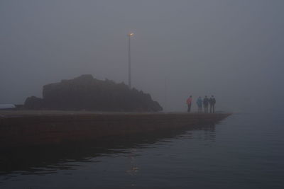 Silhouette people on illuminated sea against sky at dusk