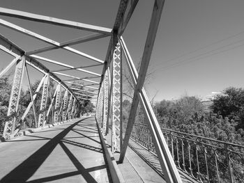 Black and white photography of a steel bridge going over a road, in the summer.  trees by the side.