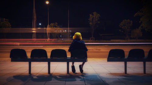 Rear view of boy sitting on chair at night