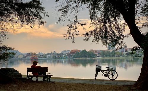 Man sitting on seat by lake against sky during sunset