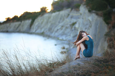 Young woman sitting by sea