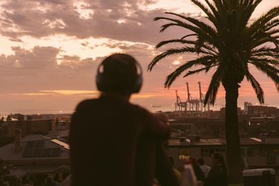 Rear view of silhouette man and cityscape against sky during sunset