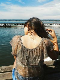 Rear view of woman standing by river against sky